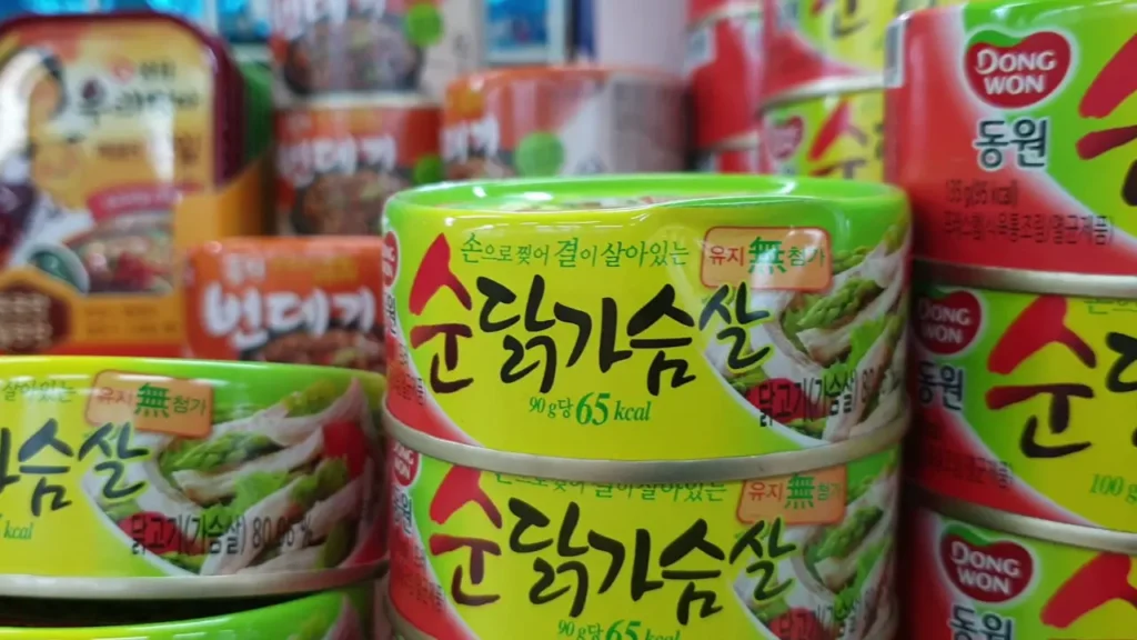 마트 진열대에 쌓여 있는 한국산 닭가슴살 통조림들. 찌그러짐과 같은 외관상 손상이 있을 수 있는 통조림의 위험성을 강조하며, 소비자에게 주의를 환기시킨다.