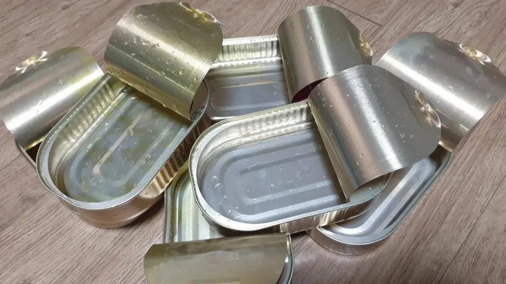 내용물을 비우고 깨끗하게 씻겨진 여러 개의 빈 통조림 캔들이 나무 바닥 위에 쌓여 있다. 이는 유통기한이 지난 비상식량을 폐기한 후의 모습이다.